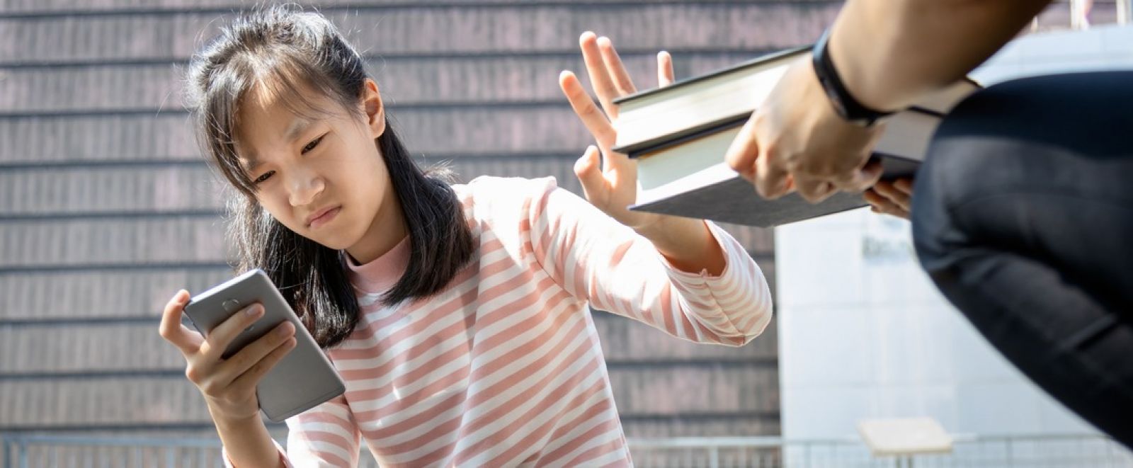 A child sitting on a wood deck with a book and a phone banner image